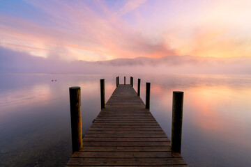 Obraz premium Wooden jetty on calm misty lake at sunrise, Derwentwater, Lake District, UK.