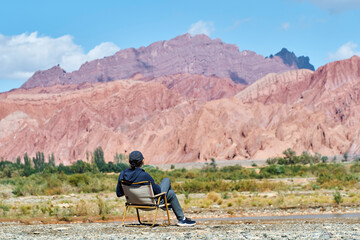 asian man sitting in a chair looking at a reddish mountain