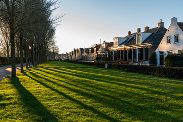 Long tree shadows stretch across a lush green park in the village of Schiermonnikoog, bathed in warm golden sunlight near sunset