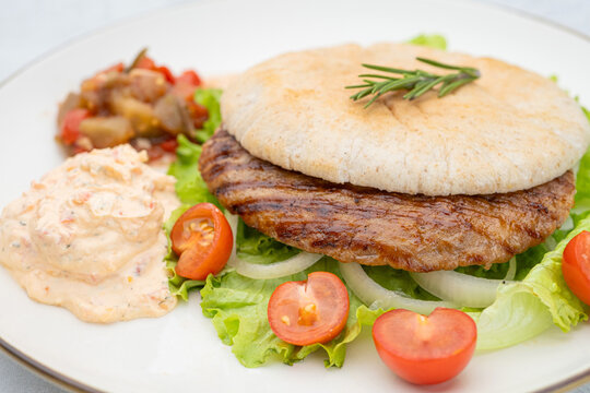 Closeup of Serbian pljeskavica served with traditional Balkan side dishes. Balkan style pljeskavica burger on a plate with Serbian urnebes salad
