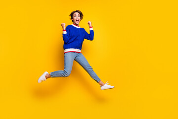Fototapeta na wymiar Full length photo of impressed funky girl wear blue pullover jumping high empty space rising fists isolated yellow color background