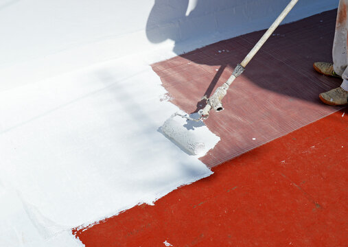 White paint on the house roof to combat the summer heat due to climate change. White rubber waterproofing paint applied with a roller to waterproof the terrace of the house. 