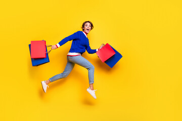 Full length photo of cheerful funny lady dressed sweater running fast holding shoppers jumping...