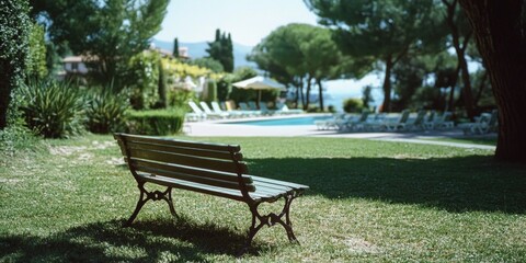 Obraz premium A peaceful outdoor scene with a sunlit bench by the grass, set against a backdrop of a resort-like area.