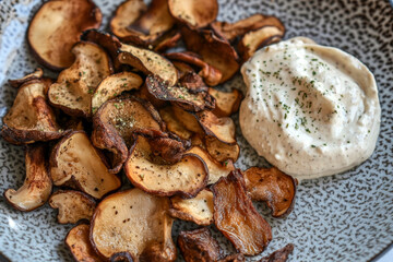 Crispy mushroom chips with creamy dip on patterned plate.