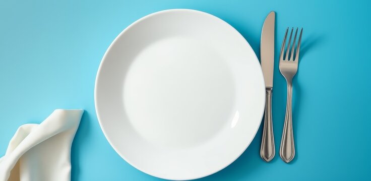 Empty white plate with fork and knife on blue background. Table setting, dining, restaurant, food preparation, and meal concept