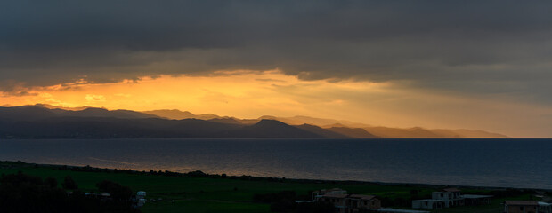 Golden sunset over distant mountains reflecting on calm waters of the coastline