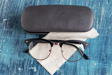 Sleek glasses in classic plastic frame with case and napkin on a blue table.