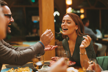 Man feeding woman delicious meal with fork while enjoying romantic dinner at restaurant