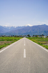 Fototapeta premium Ohisama road and Mount Jonen | Scenic Spring Landscape with a Straight Road and Snow-Capped Japanese Alps in Azumino, Nagano, Japan 