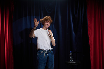 Performer delivering stand-up comedy on stage with microphone in hand, engaging audience with humor...