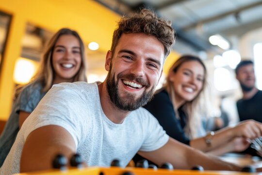A smiling group plays foosball in a brightly lit office, capturing energy and happiness that arises from fun interactions and teamwork among young professionals in a relaxed setting.
