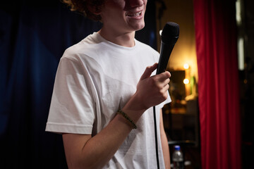 Person holding microphone on stage, performing in front of an audience in a dimly lit venue with...