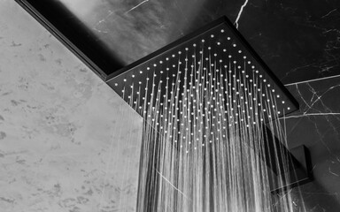 A sleek black square rain shower head mounted on the wall in a modern bathroom interior, combining...