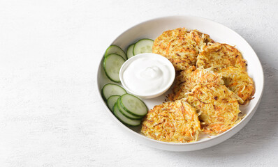 Crispy cabbage pancakes with sour cream and fresh cucumber slices on white plate