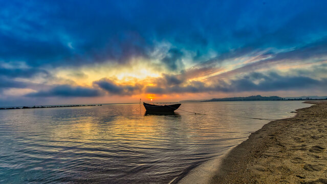 Fishing boat at sunset after a day of work bobbing in the shallow water and waves on the beach of a small bay