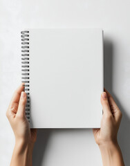 blank white spiral notebook being held by two hands, against a white background