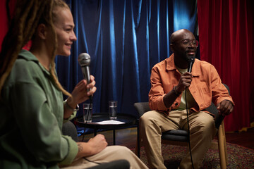 Two individuals discussing lively topics while recording a podcast in a cozy studio setting....