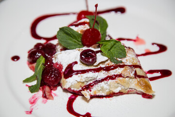 Cake with cherries and mint on a white plate in a restaurant.