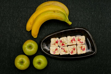  Sushi roll with cream cheese and fruit on a black plate with banana and apple on a black background