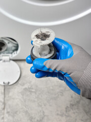 Plumber in gloves holding washing machine filter in hand. Checking dirty clogged drain pump filter.