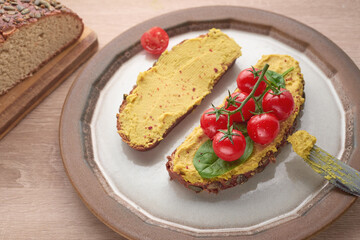Delicious brunch hummus toast served on a white plate with cherry tomatoes and aromatic herbs. 