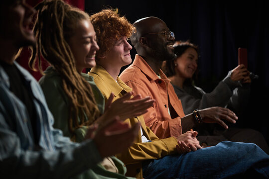 Group of diverse individuals seated in a theater, enjoying and applauding a performance on stage. Their cheerful expressions highlight appreciation and excitement for the act