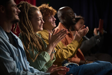 Fototapeta premium Group of diverse people sitting in row and applauding during a performance, capturing joy and engagement, showcasing various ethnic backgrounds and unity