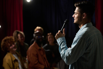 Comedian delivering his routine on stage, entertaining an engaged audience who are smiling and...
