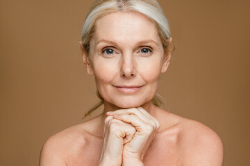Portrait of attractive mature woman with beautiful smooth skin smiling at camera, lady touching...