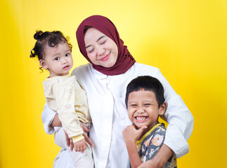 A joyful asian mother holds her two happy children against a bright yellow background. mothers day concept
