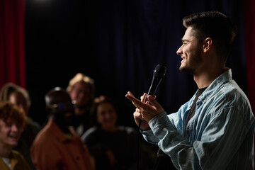 Man holding a microphone engaging audience in a dimly lit room, with focused expressions from...