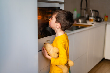 A cute boy in a yellow blouse looks into the oven where an apple pie is being prepared. Homemade...