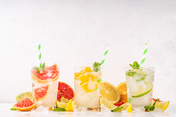 Set of summer citrus infused detox water drinks, lemon, lime, grapefruit, orange, lime iced lemonade drinks on white wooden background. Iced seasonal refreshment beverages, with fruit slices and mint