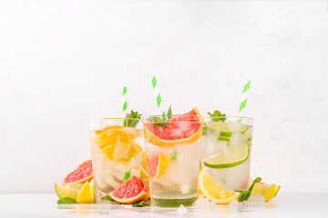 Set of summer citrus infused detox water drinks, lemon, lime, grapefruit, orange, lime iced lemonade drinks on white wooden background. Iced seasonal refreshment beverages, with fruit slices and mint