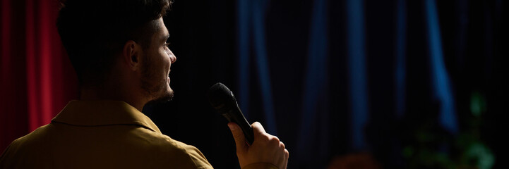 Comedian performing stand-up comedy on stage while holding microphone in hand, background curtains...