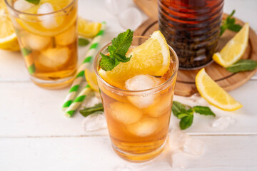 Iced tea cocktail drink, cold summer drink with black tea, lemon, mint and crushed ice, tasty refreshing non-alcohol mocktail on white wooden table background 
