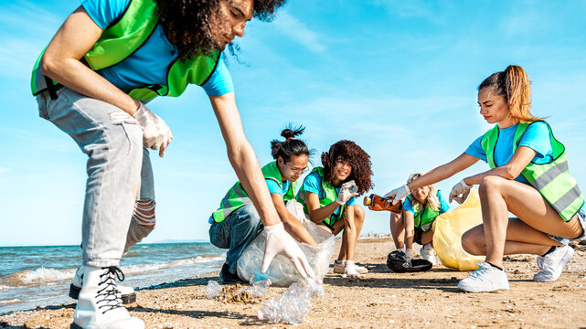 Group of eco volunteers picking up plastic trash on the beach - Activist people collecting garbage protecting the planet - Ocean pollution, environmental conservation and ecology concept.