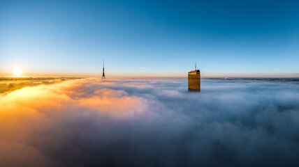 Thick fog covering Riga city in colorful sunrise colors. Drone view over old town, TV tower and...