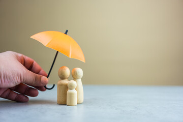 Someone hand holding orange umbrella protects a family of wooden peg dolls. Insurance concept. Family and health insurance with copy space
