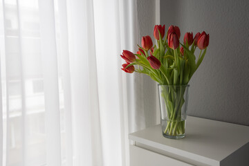 Bouquet of red tulips in a glass vase on a white table