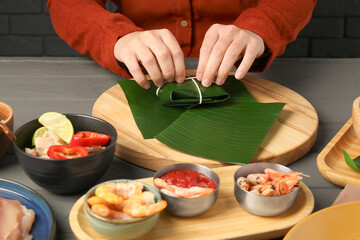 Woman tying banana leaf with food at wooden table with products, closeup. Healthy eco serving