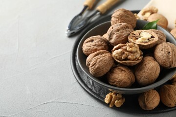 Fresh walnuts in bowl and nutcracker on gray textured table, closeup. Space for text