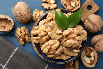Fresh walnuts and green leaves in bowl on blue wooden table, flat lay