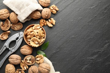 Fresh ripe walnuts, shells and nutcracker on black table, flat lay. Space for text