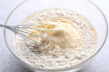 Whisk and bowl of dough on grey table, closeup
