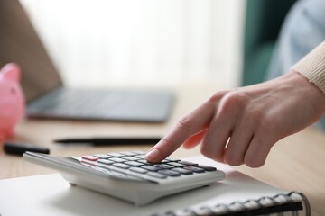 Budget. Woman with calculator, paperwork and laptop at wooden desk indoors, closeup