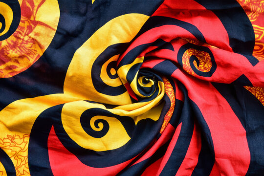 Bright Kenyan Kitenge fabric, bold swirling red, orange, and yellow patterns in a wax-dyed cotton weave.