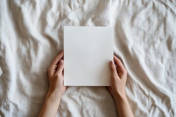 Hands holding blank white square paper on linen fabric.