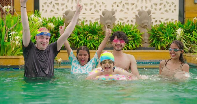 Indian happy family group with teen child look cam do funny pose enjoy outdoor resort pool trip Asian dad man mal young adult girl boy female have fun joy spend day time at outside water park villa